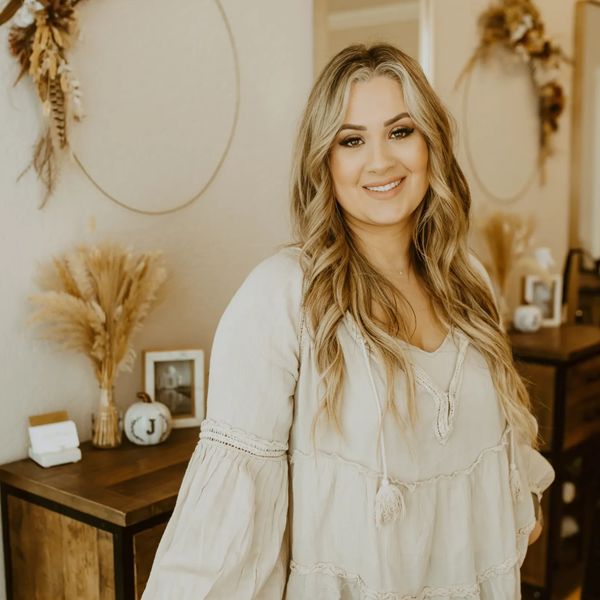 Smiling woman with long blonde hair in a cozy, neutral-toned room.