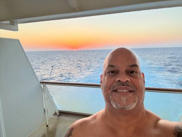 Man smiling on a ship balcony during sunset at sea.