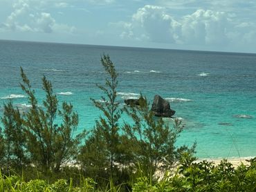 Turquoise ocean with rocks and coastal greenery under a partly cloudy sky.