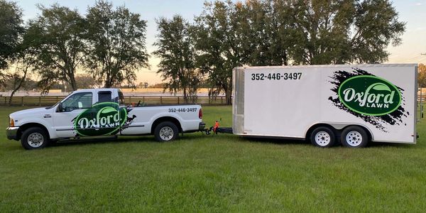 Oxford Lawn truck and trailer parked on green grass with trees in background.