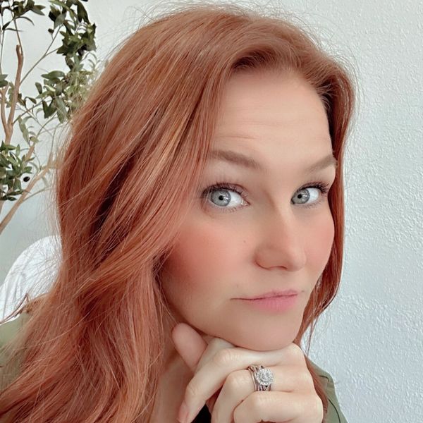 Woman with red hair and blue eyes rests chin on hand.