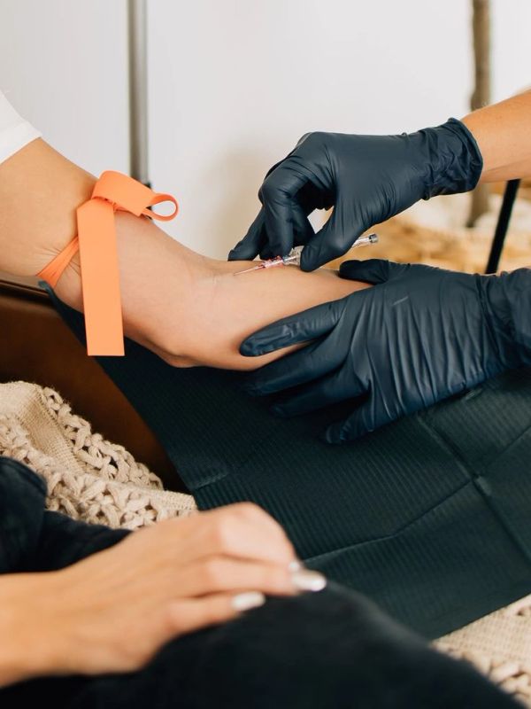 Blood is being drawn from a patient's arm with a needle and tourniquet.