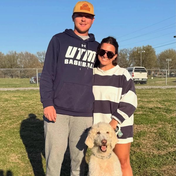 A couple with a large fluffy dog outdoors on a sunny day.