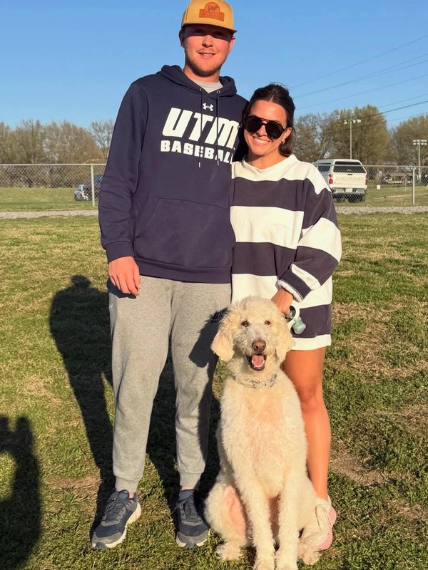 A couple with a large fluffy dog outdoors on a sunny day.