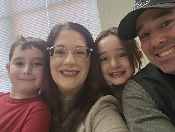 Smiling family selfie with two kids and parents indoors.