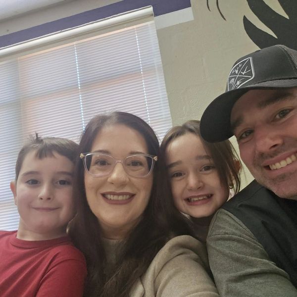 Smiling family selfie with two kids and parents indoors.