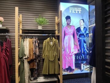Clothing rack with dresses and coats next to a fashion poster in a store.