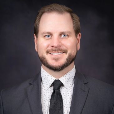 Professional man in suit smiling against a dark background.