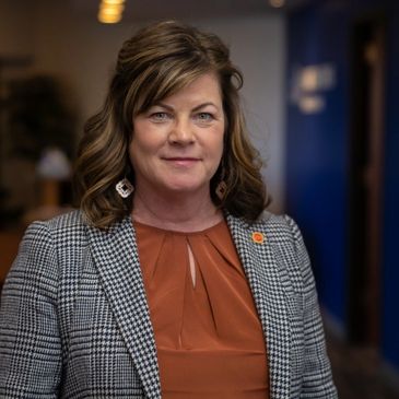 Professional woman in a checkered blazer and rust-colored blouse.