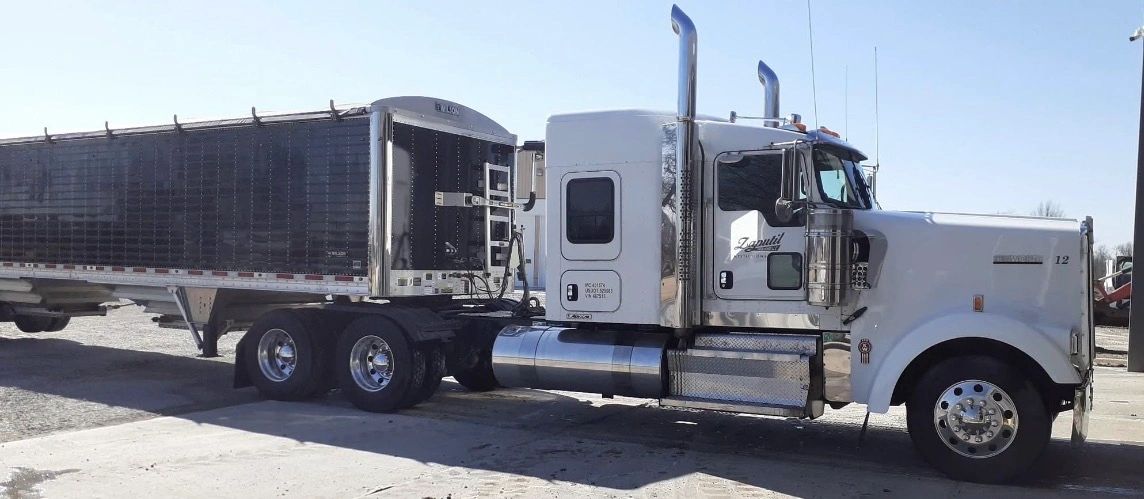 A white semi-truck with a black trailer parked on concrete under a clear sky.