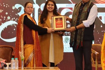 Group on stage presenting an award plaque at an event with traditional attire.
