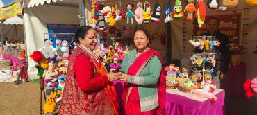 Two women exchanging a handmade flower pot at a colorful craft market stall.