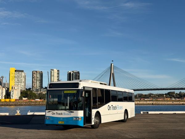 A white and blue On Track Buses vehicle parked by the waterfront under a clear sky.