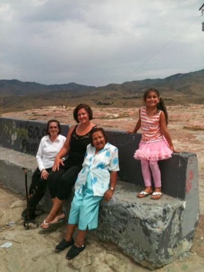 Angie sits on a concrete bench between 2 elderly Mexican women with her 8-year-old daughter smiling.