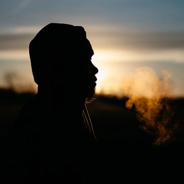 Silhouette of a person exhaling vapor at sunset.