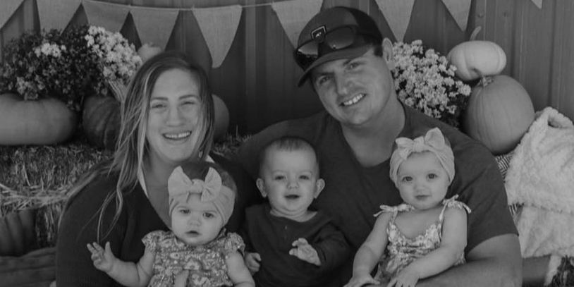 A happy family with two parents and three babies posing in a festive autumn setting.