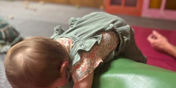 A toddler leaning over a green cushion indoors.