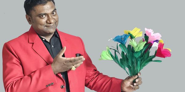 Man in red blazer holding colorful artificial flowers and gesturing.