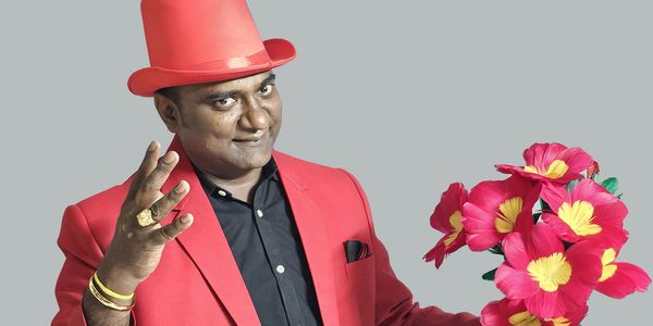 Man in red suit and hat holding pink flowers, making a gesture.