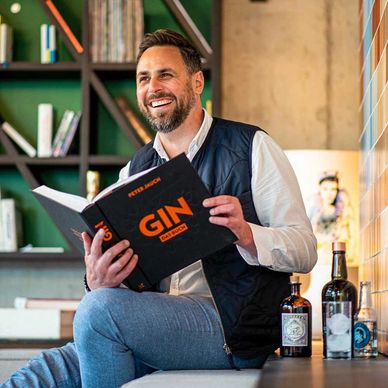 Peter Jauch with his book “GIN – Das Buch”, surrounded by premium gin bottles in a modern setting.