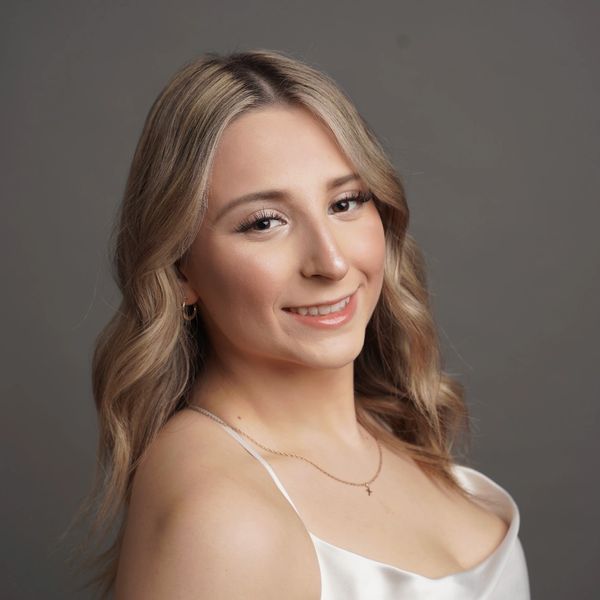 Young woman with blonde hair smiling against a neutral background.