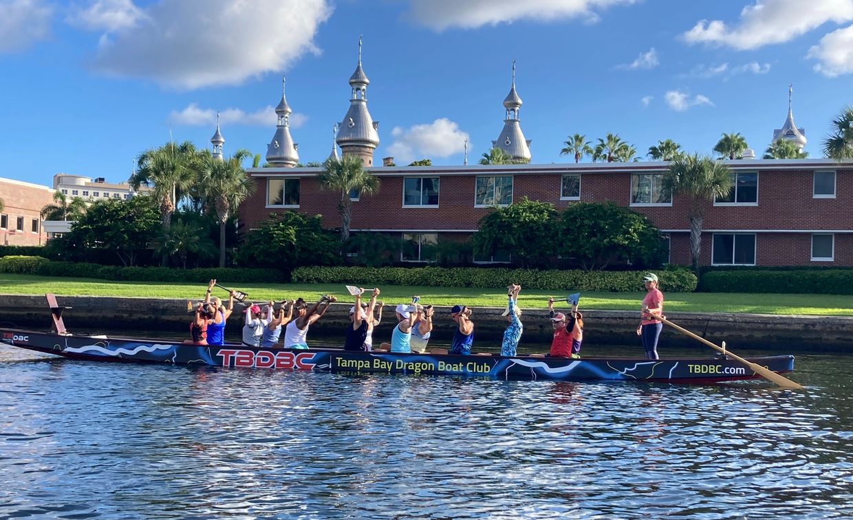 Members of the  Tampa Bay Dragon Boat Club  in a dragon boat  with the University of Tampa in the ba