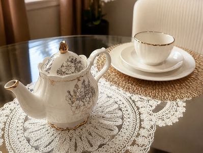 Elegant floral teapot and teacup set on lace and rattan mats.