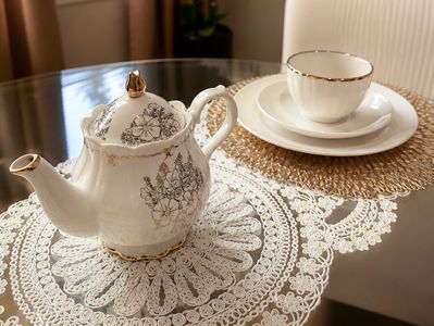 Elegant floral teapot and teacup set on lace and rattan mats.