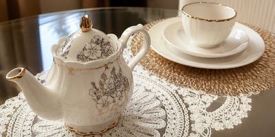 Elegant silver-trimmed teapot and teacup set on lace doilies.