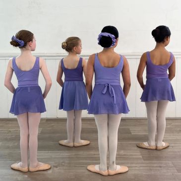 Four girls in lavender ballet outfits standing back to camera.