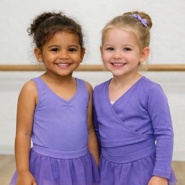 Two young girls smiling in purple ballet outfits.