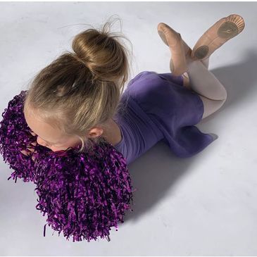 Young ballet dancer in purple outfit lying down with pom-poms.