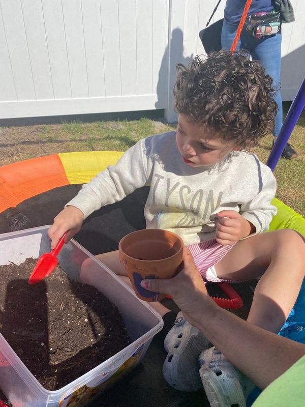 Child playing with soil and a red shovel outdoors in a colorful play area.