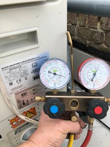 Hand holding HVAC manifold gauge set near an air conditioning unit.