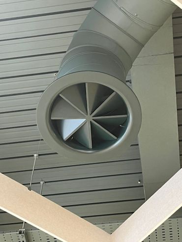 Ceiling air duct with a circular vent and segmented blades.