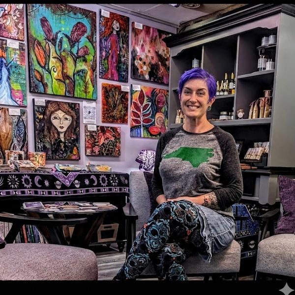Woman with purple hair sitting in an art-filled room with colorful paintings.