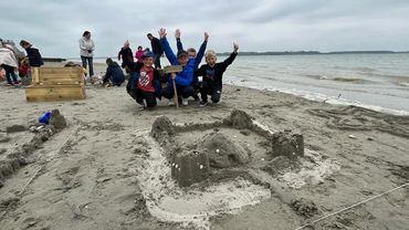 Les enfants posent devant leur château de sable.