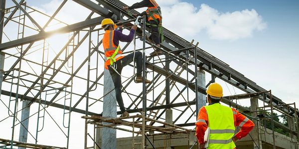 Construction workers installing roofing structure on a building frame under clear sky.