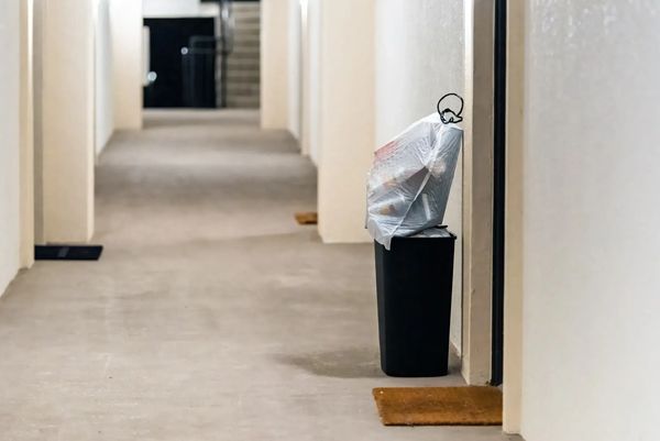 Trash bag overflowing on a black bin in a hallway.
