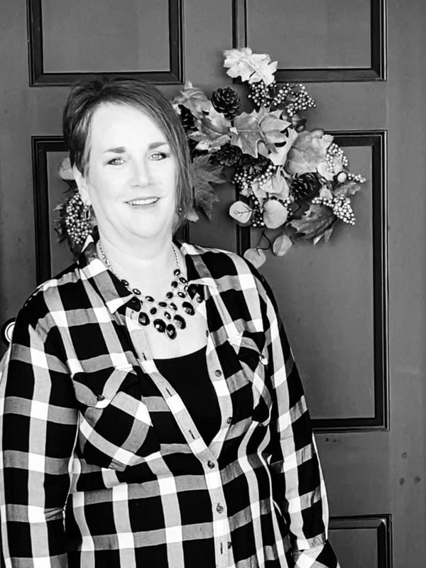 Woman smiling in a checkered shirt standing by a decorated door.
