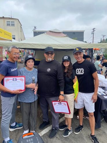 Five people posing with certificates at an outdoor event under cloudy skies.
