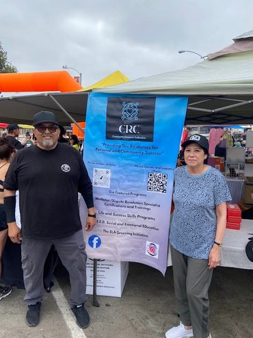 Two people standing beside a Community Resource Collective banner at an outdoor event.