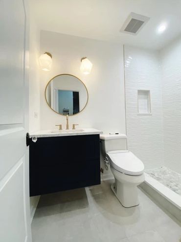 Modern bathroom with a round mirror, dark vanity, and white toilet.