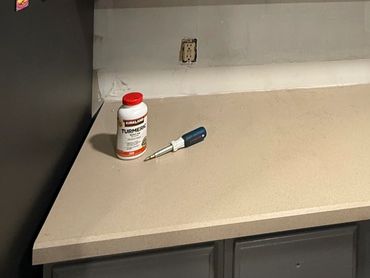 A kitchen counter with a turmeric bottle, screwdriver, and some plastic containers.