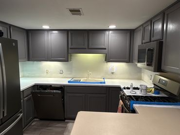 Modern kitchen with gray cabinets and stainless appliances under recessed lighting.