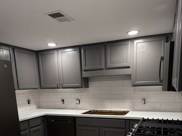 Modern kitchen with gray cabinets and white countertops, under cabinet lights.