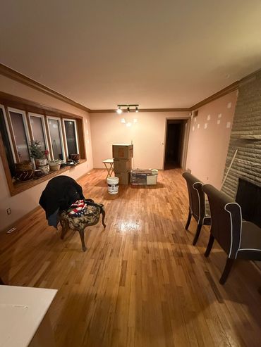 Living room with wooden floors, a few chairs, and stacked boxes in the center.