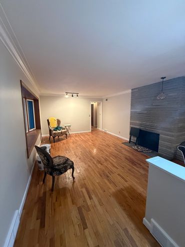 Spacious living room with wooden floors, vintage chairs, and a stone fireplace.