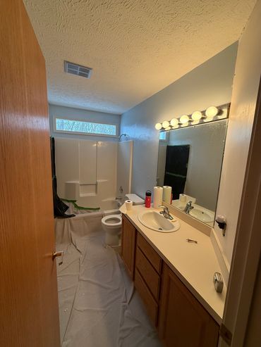 Bathroom under renovation with protective covering on the floor and taped tub area.