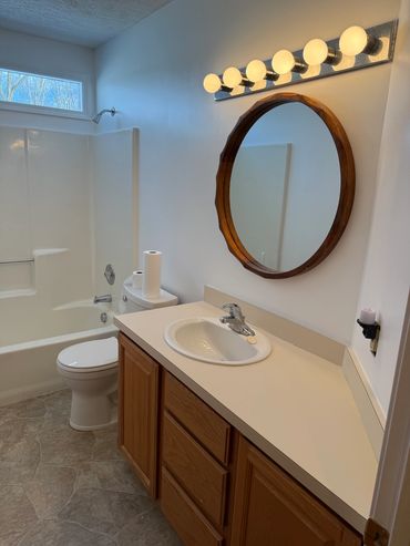 Simple bathroom with wooden vanity and round mirror.